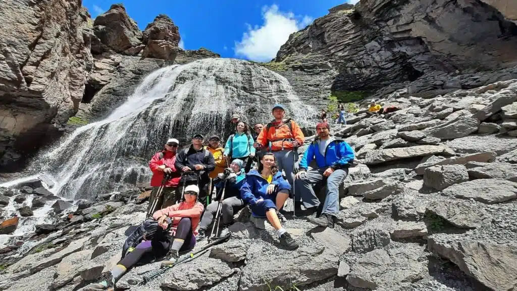 A group of climbers in mountain gear stands before a stunning waterfall.