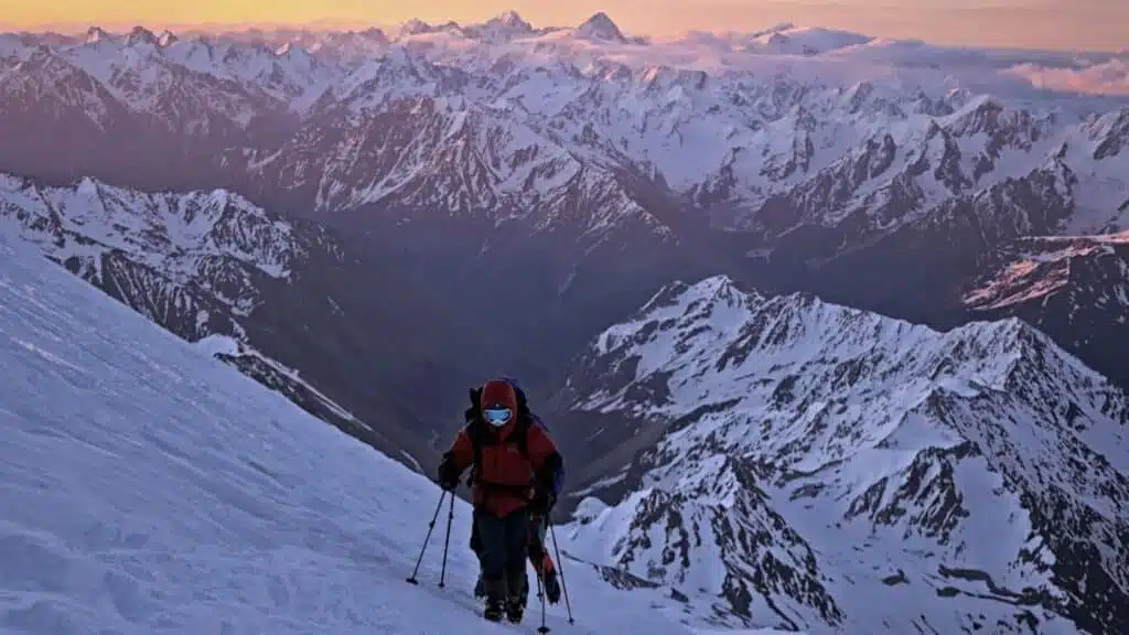 Climber ascends Elbrus at dawn, with fiery peaks behind - B4Experience.