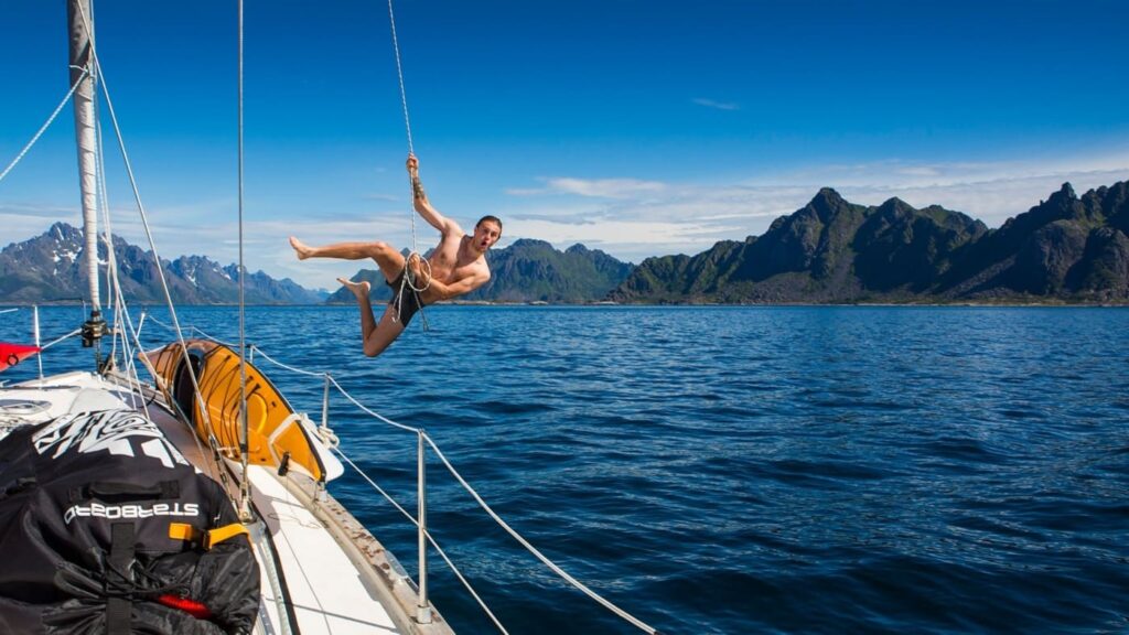 Man doing Tarzan with one of the ropes of the sailboat to end up in the water