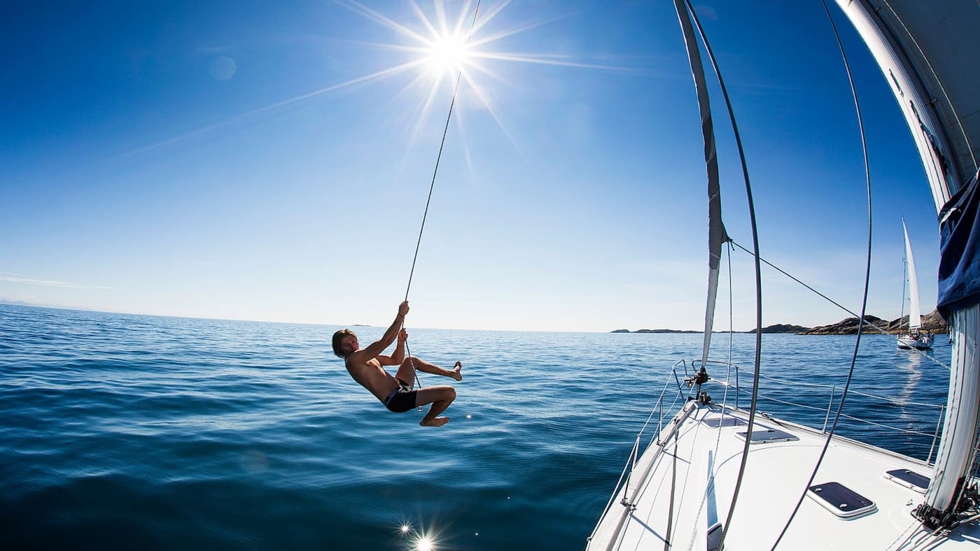 Man doing Tarzan with one of the ropes of the sailboat to end up in the water