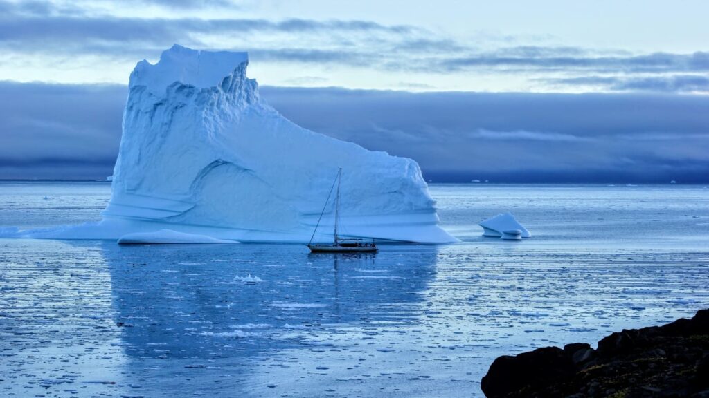 Sailboat anchored next to a large iceberg