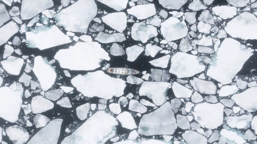 Aerial view of a sailboat surrounded by ice blocks in the Arctic Circle