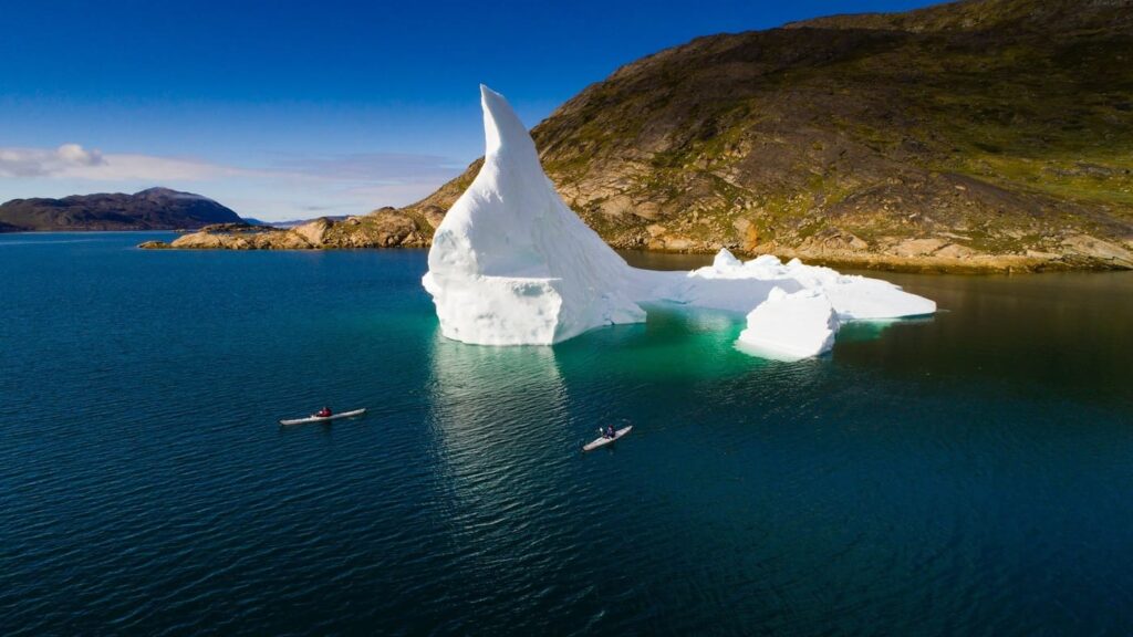 Kayaks sailing alongside ice floes in Svalbard in summer