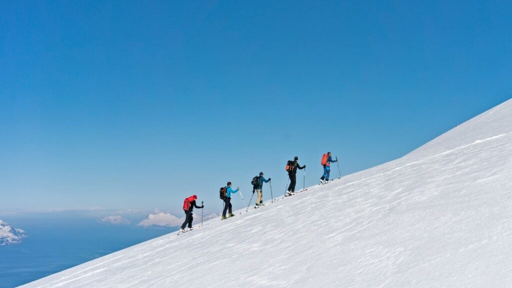 Skiers climb snowy mountain for big descent