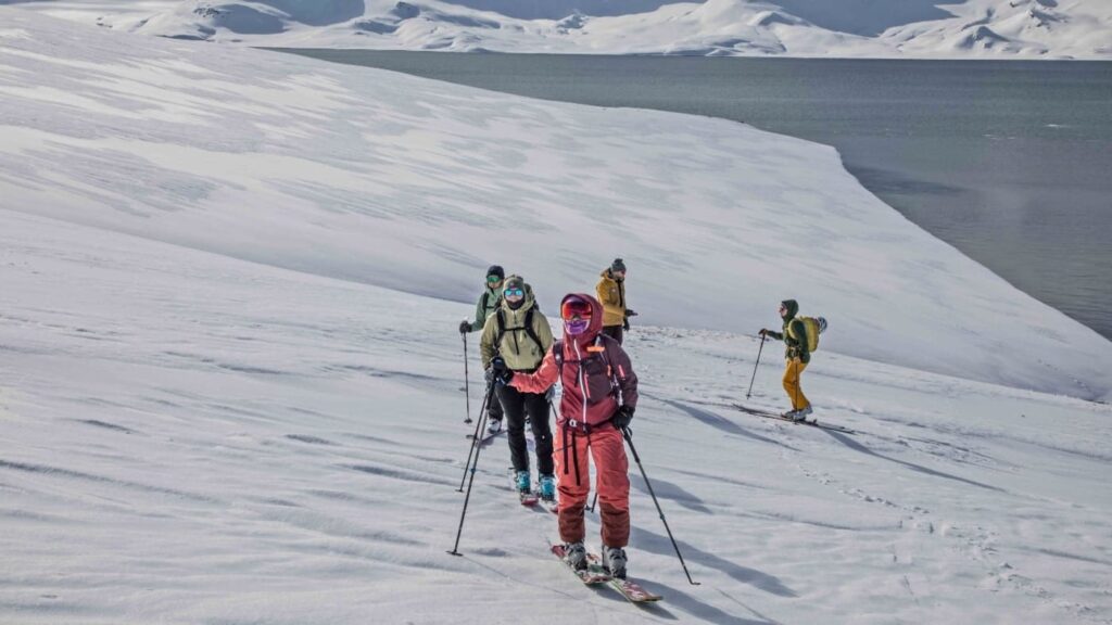 Group of skiers begins the ascent of a snowy mountain, views of the sea in the background