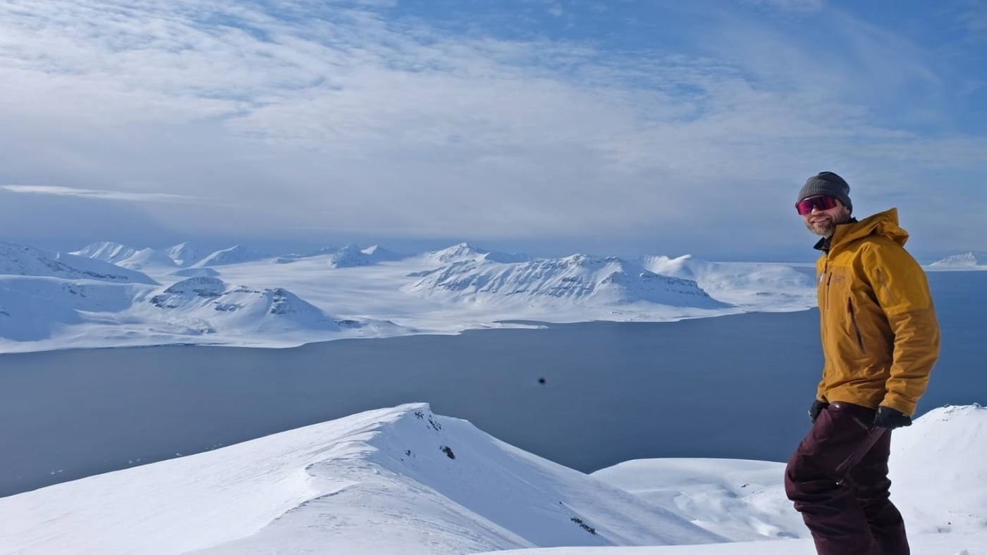 Smiling skier poses on the summit with incredible views in Svalbard