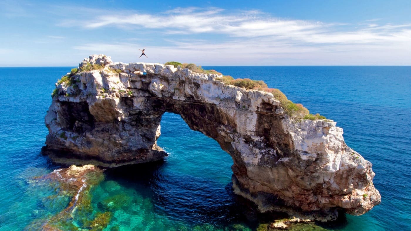 A climber stands atop Es Pontàs, a natural rock arch in Mallorca with B4Experience