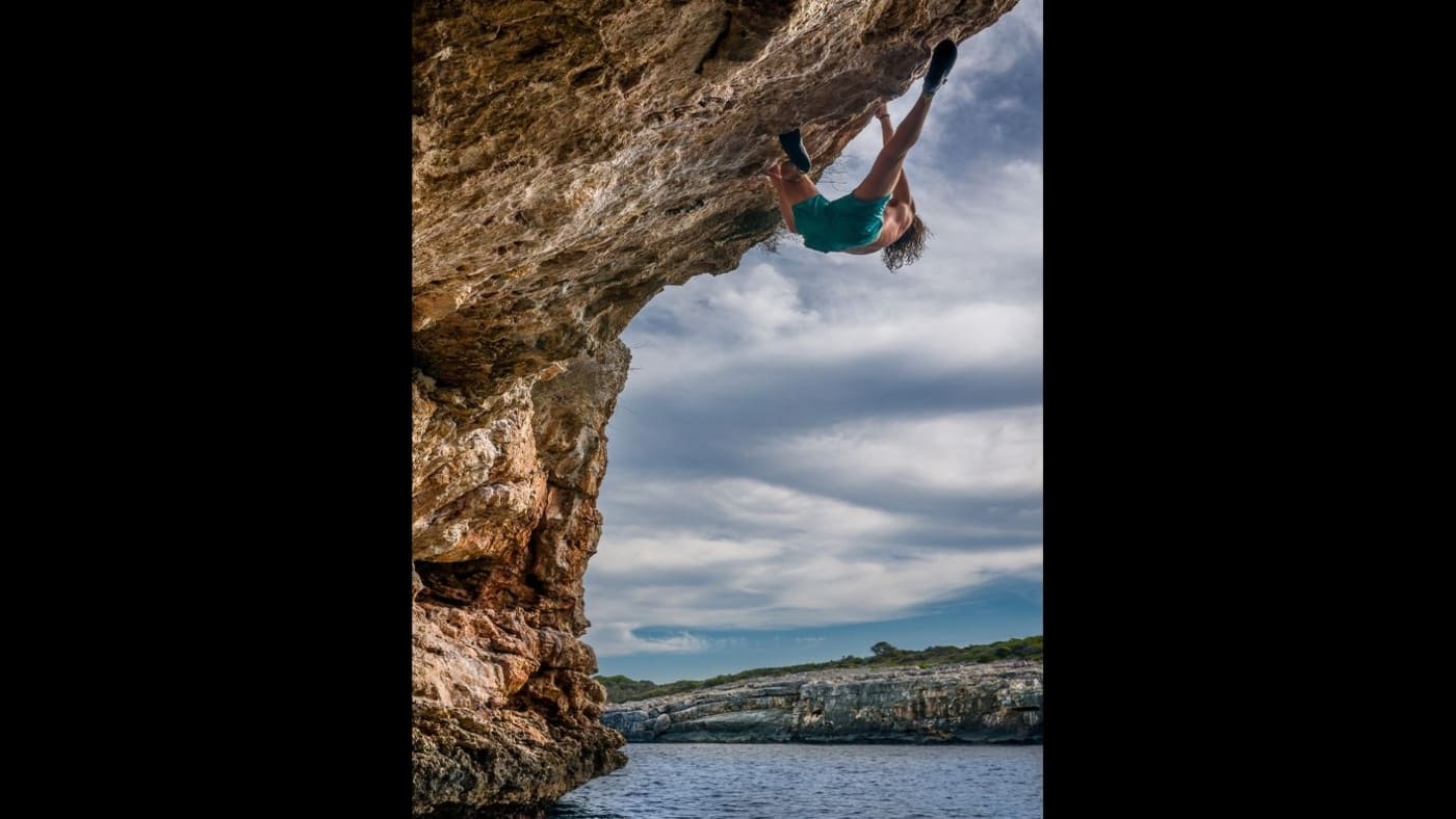 A climber free solos over deep water on a coastal overhang with B4Experience