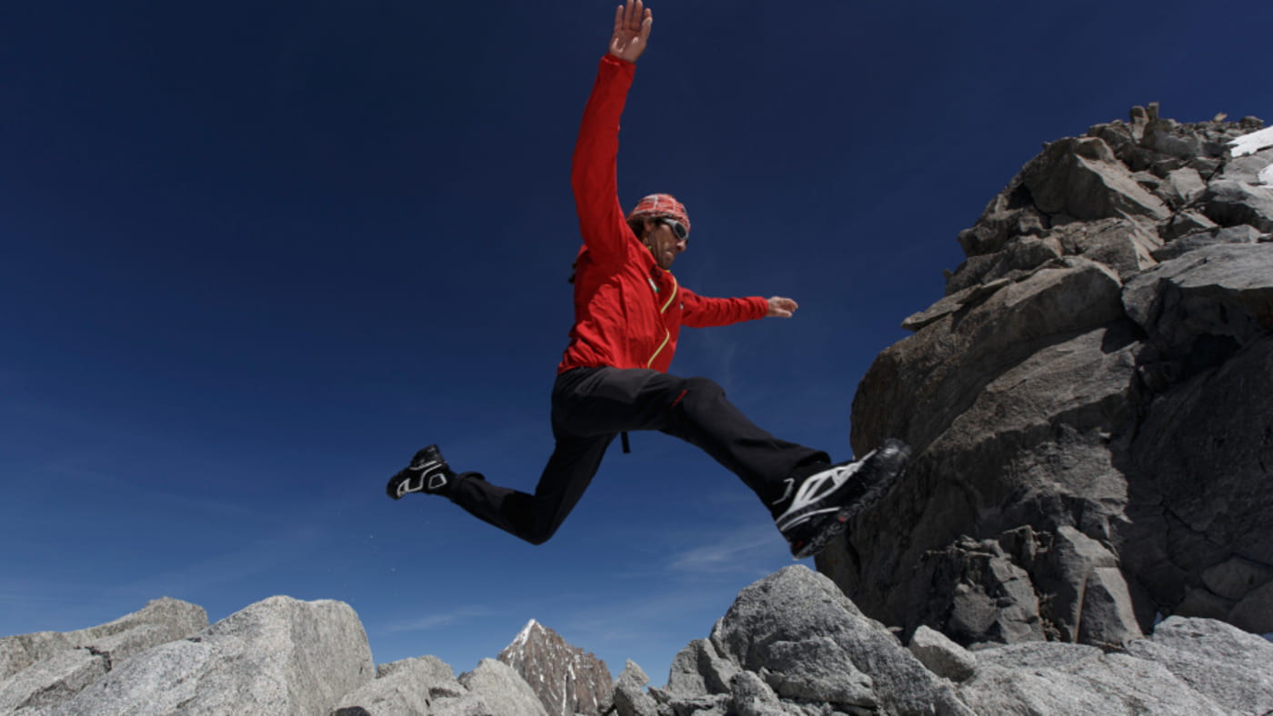 Jordi Tosas leaping over rugged mountain terrain under a clear blue sky with B4Experience