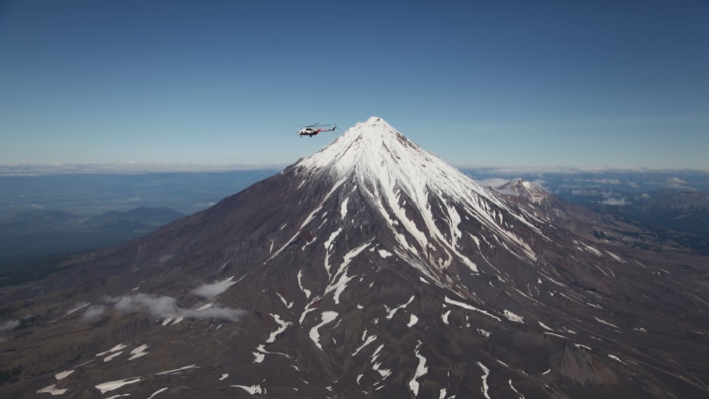 A helicopter flies over towering Kamchatka volcano with B4Experience