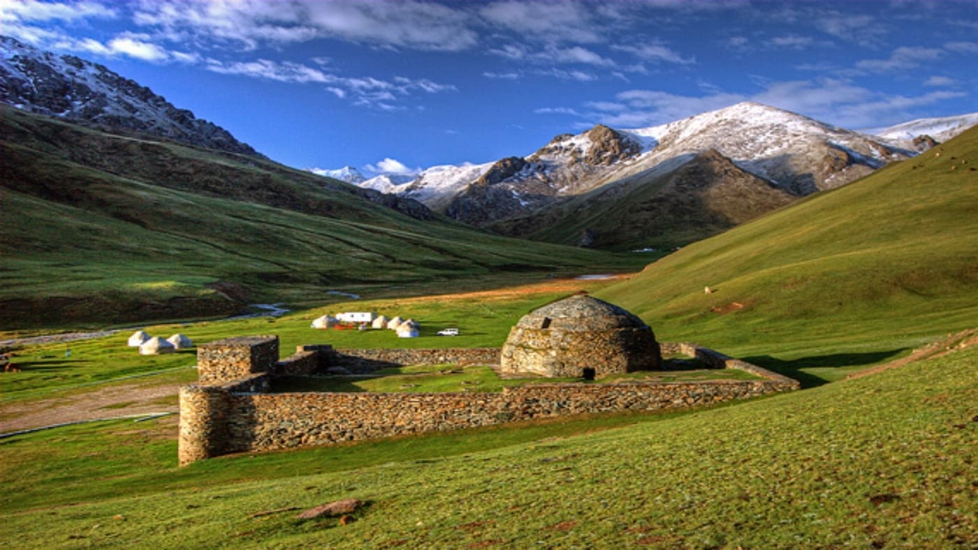 Scenic view of Kyrgyzstan's mountains with traditional stone structures in a green valley with B4Experience