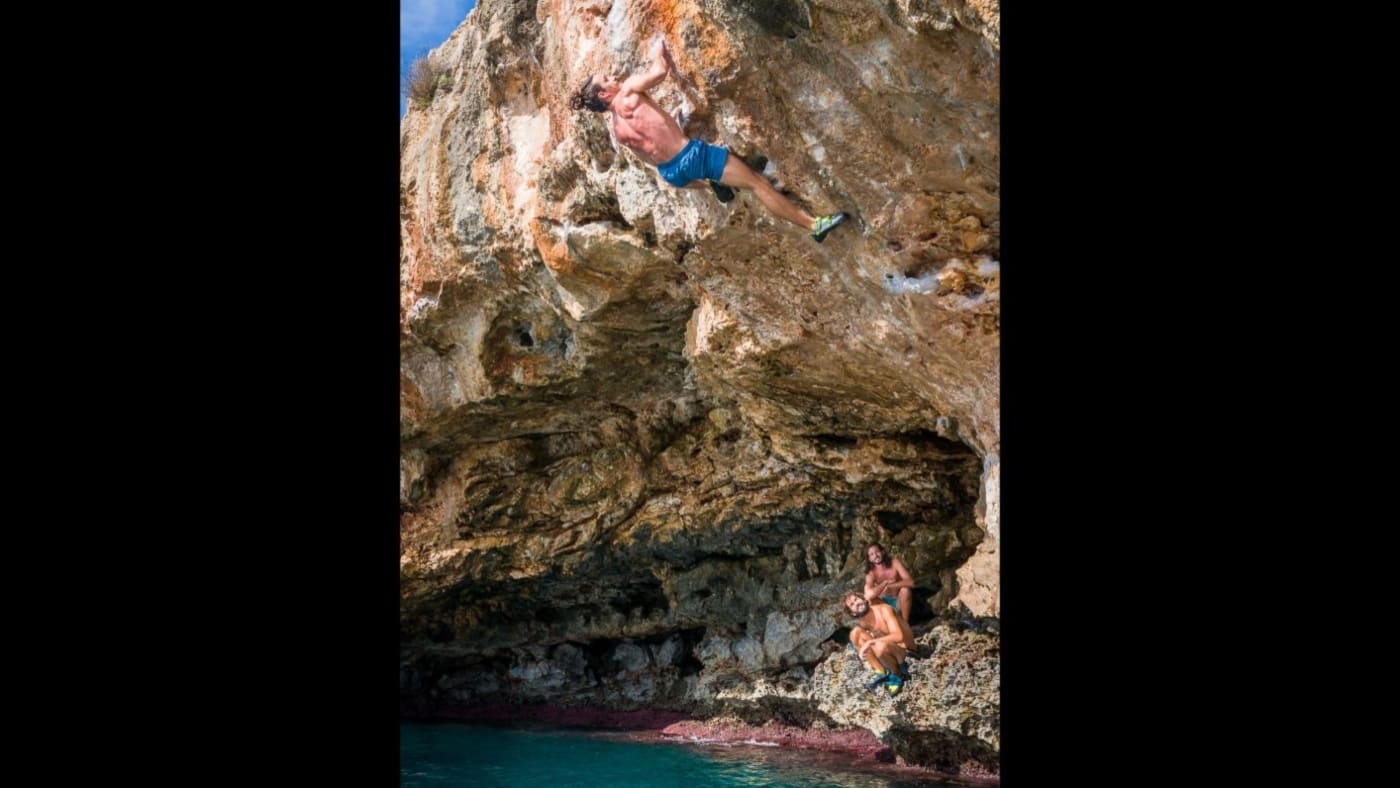 A climber deep water soloing on Mallorca's rugged sea cliffs with B4Experience