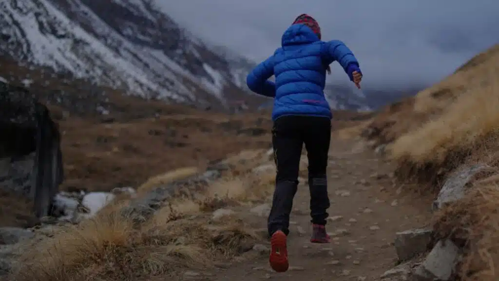 Trail runner in a blue jacket navigating a rugged mountain path in Nepal - B4Experience