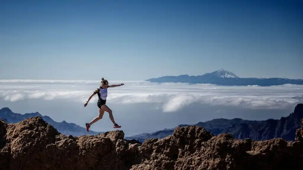 Trail runner leaping over rocky terrain above the clouds.