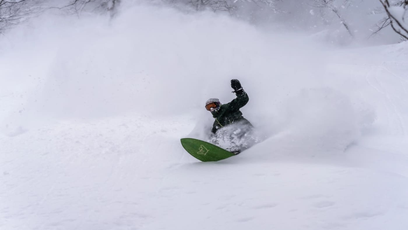 Snowboarder caving through deep powder in a snowy forest with B4Experience