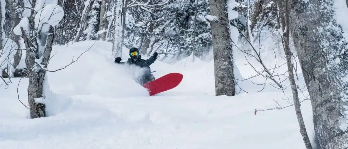 Snowboarder riding through deep powder in a snowy forest in Japan with B4Experience
