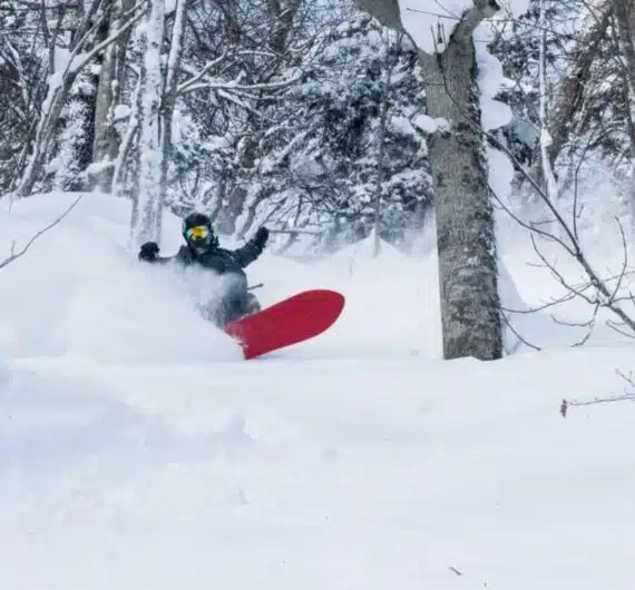 Snowboarder riding through deep powder in a snowy forest in Japan with B4Experience