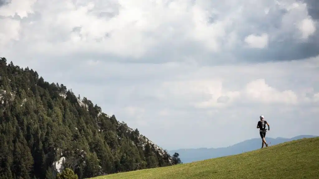 Lone trail runner on a grassy hill with forested slopes with B4Experience