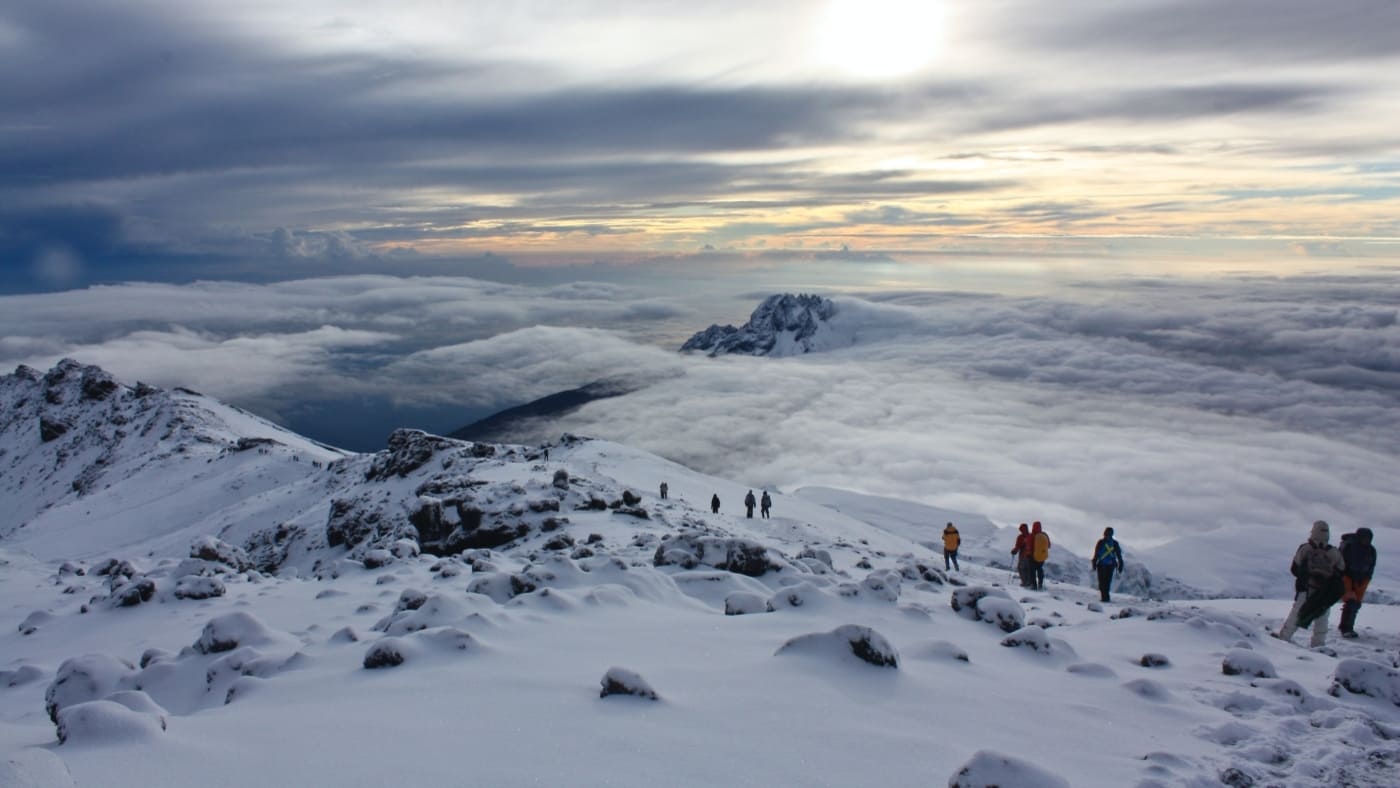 Trekkers traverse Kilimanjaro's snowy summit at sunrise with B4Experience