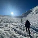 Two climbers trekking up a snowy slope under a bright sun - B4Experience
