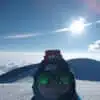 A snowmobile rides under the bright sun on a mountain ridge - B4Experience