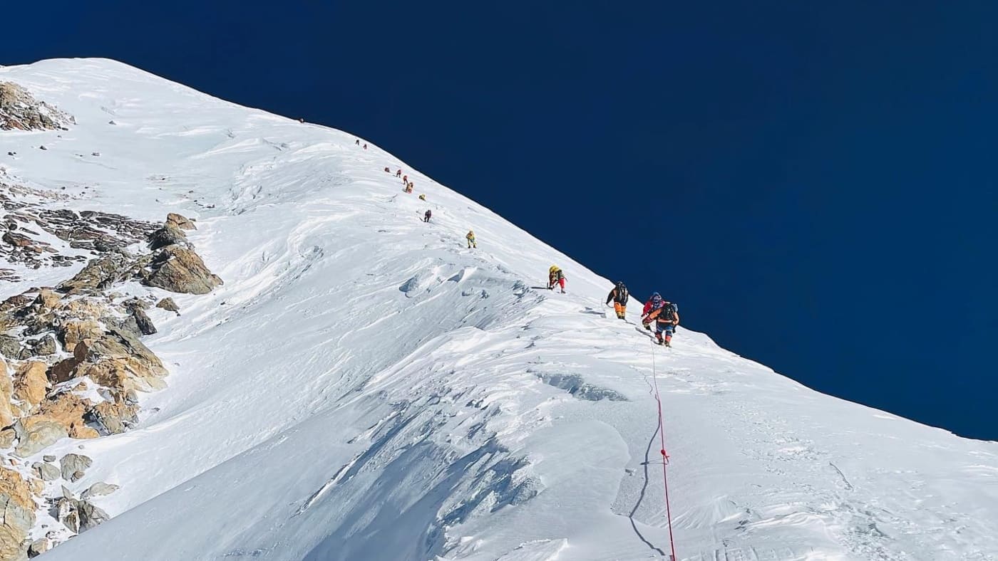 A team of climbers follows a steep, snowy ridge on their ascent of K2 - B4Experience