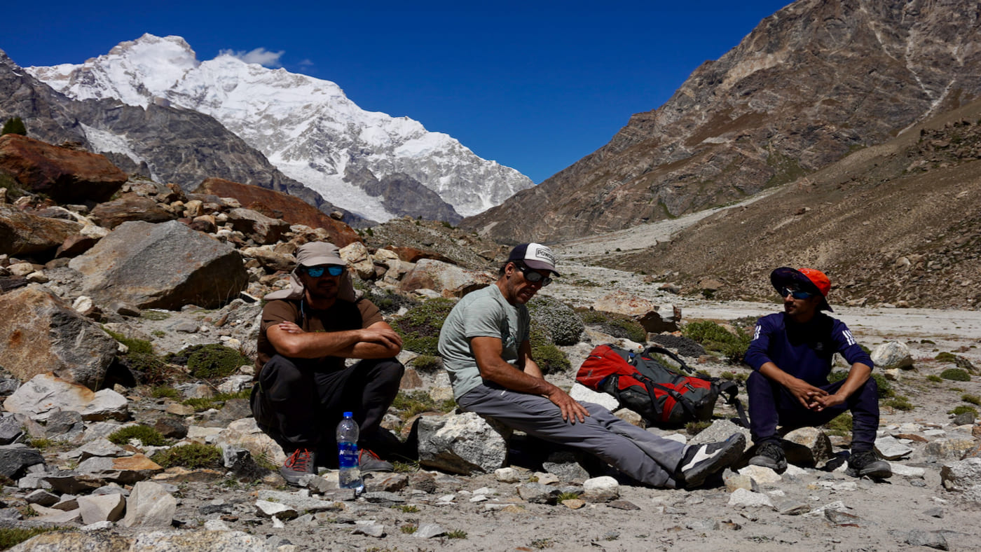 Group of trekkers resting on rocky terrain with a stunning snow-capped mountain backdrop - B4Experience