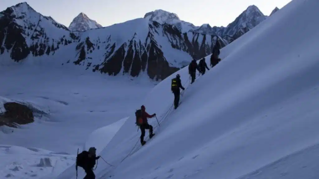 Group of climbers ascending a steep, snowy ridge with breathtaking mountain peaks in the background - B4Experience