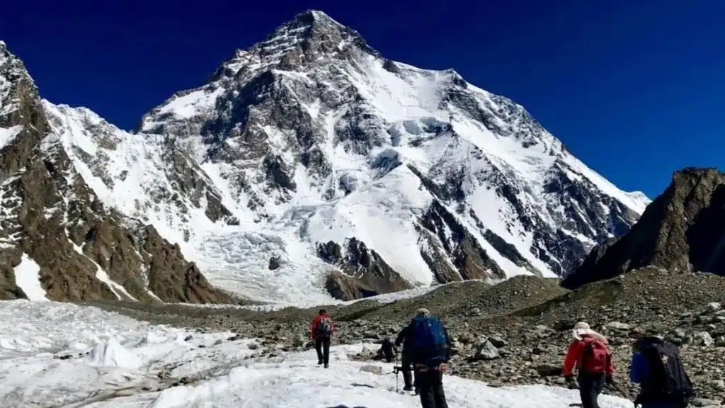 Trekkers making their way across a glacial landscape towards the towering, snow-covered K2 peak - B4Experience