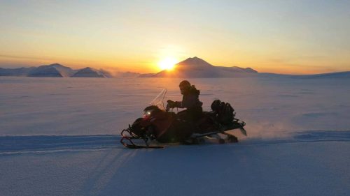 Snowmobile crossing Svalbard glacier at sunset